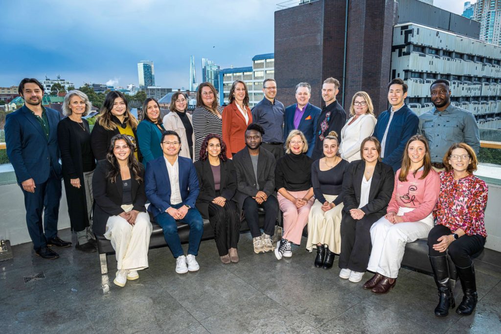 Picture of the impactinstitute team. There are 22 people pictured sitting or standing on a balcony. We are all smiling at the camera.